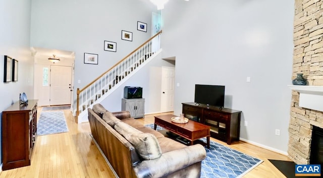 living room featuring light wood-style flooring, a fireplace, baseboards, stairway, and a high ceiling