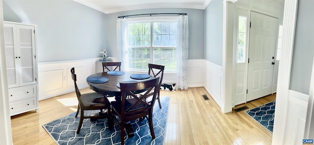 dining room with wood finished floors, a decorative wall, a wainscoted wall, visible vents, and crown molding