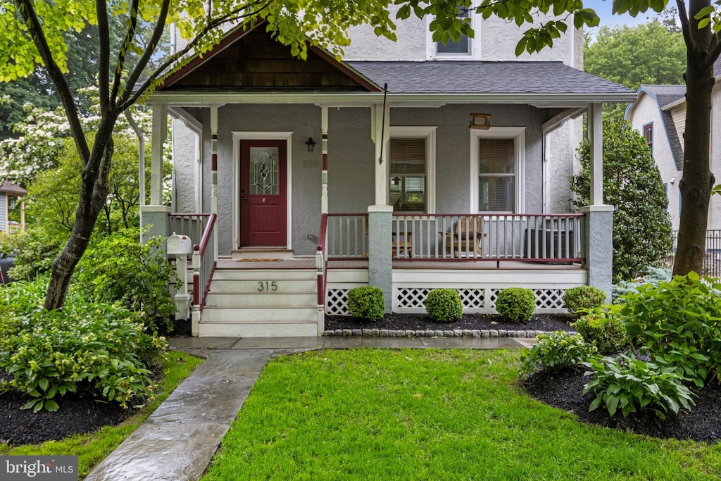 315 Vassar Ave, Swarthmore, PA 19081 - view of front of home with stucco siding, covered porch, a front lawn, and roof with shingles