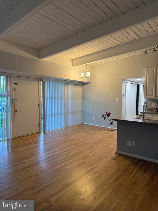 unfurnished living room featuring baseboards, beamed ceiling, light wood-style flooring, and a sink