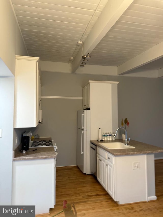 kitchen with freestanding refrigerator, white cabinets, light wood finished floors, a sink, and beam ceiling