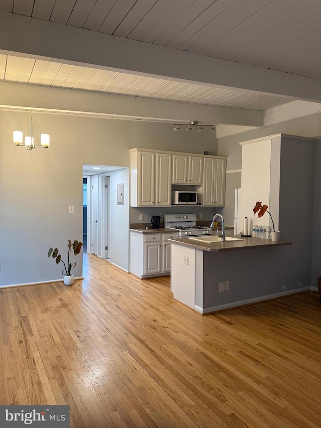 kitchen with stainless steel microwave, a sink, dark countertops, white range with gas stovetop, and light wood finished floors