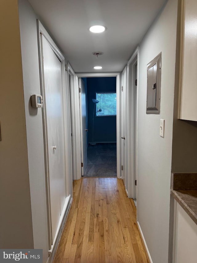 corridor featuring light wood-type flooring, recessed lighting, electric panel, and baseboards