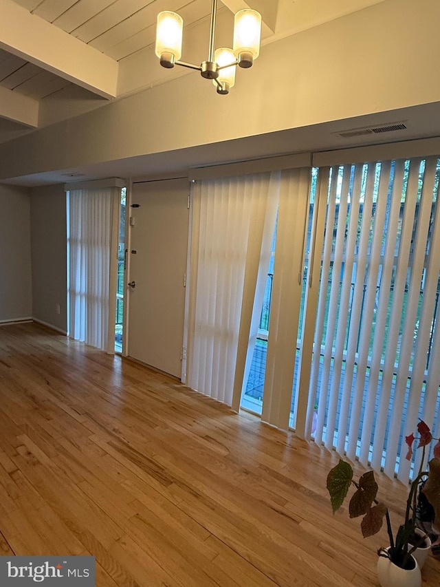 unfurnished room with beam ceiling, visible vents, wood finished floors, and an inviting chandelier