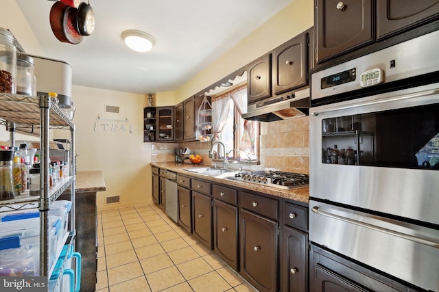 kitchen with a sink, under cabinet range hood, a warming drawer, stainless steel appliances, and light tile patterned flooring