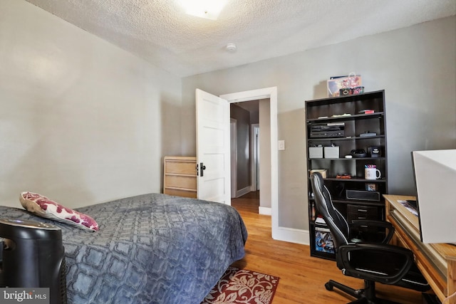 bedroom with baseboards, a textured ceiling, and wood finished floors