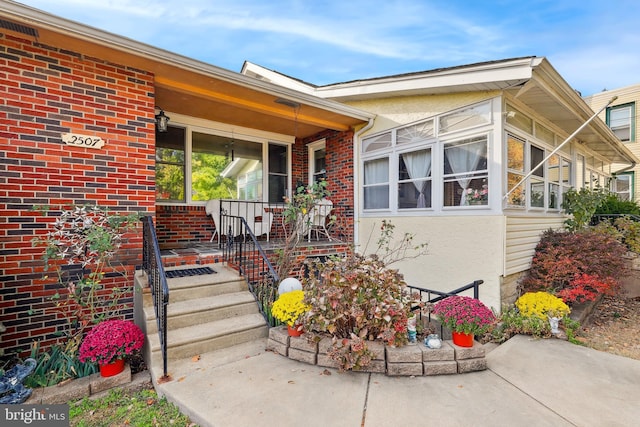 view of exterior entry with covered porch and brick siding