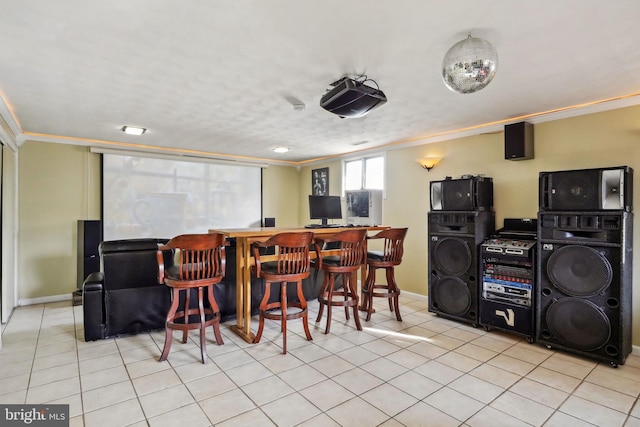 home theater room with crown molding, baseboards, light tile patterned floors, and a bar