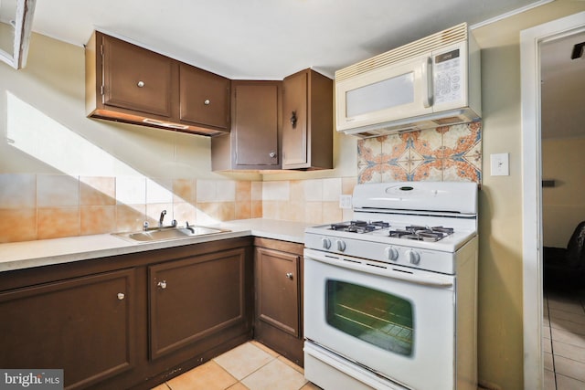 kitchen with decorative backsplash, light tile patterned flooring, white appliances, light countertops, and a sink