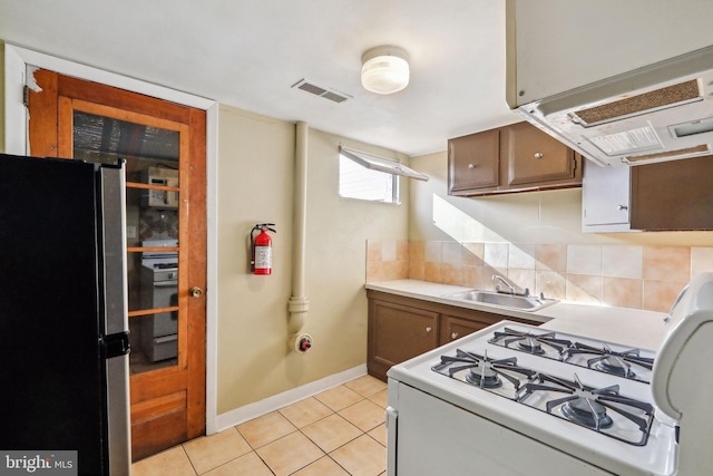 kitchen featuring light tile patterned flooring, a sink, freestanding refrigerator, decorative backsplash, and visible vents