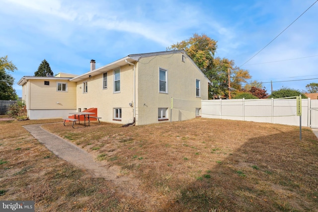 back of property with a lawn, fence, stucco siding, and a chimney