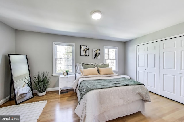 bedroom with baseboards, multiple windows, a closet, and light wood-style flooring