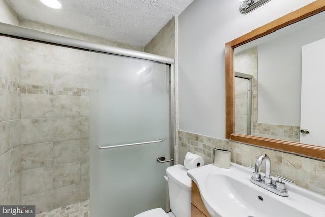 bathroom with vanity, toilet, a textured ceiling, tile walls, and a stall shower
