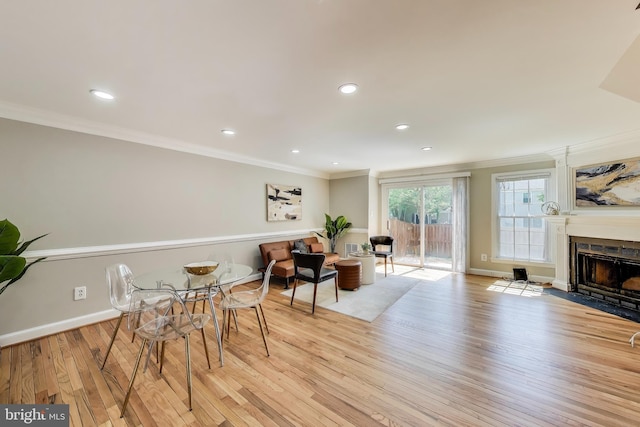 dining room featuring crown molding, a fireplace with flush hearth, baseboards, light wood finished floors, and recessed lighting