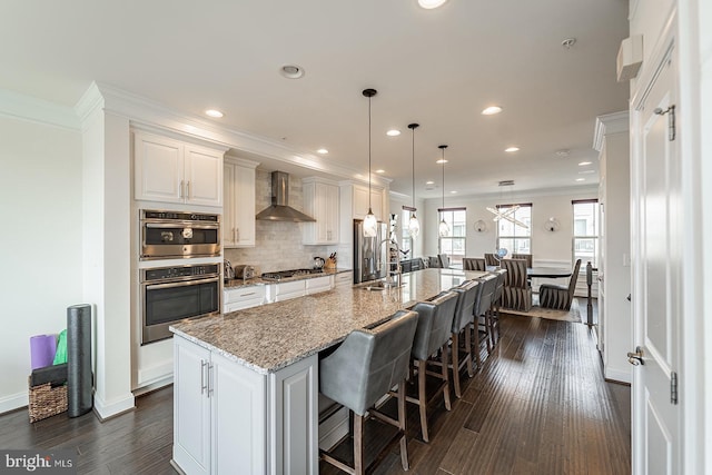 kitchen featuring a sink, a large island with sink, recessed lighting, wall chimney exhaust hood, and stainless steel gas cooktop