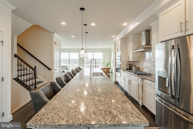 kitchen with a sink, appliances with stainless steel finishes, a large island, wall chimney exhaust hood, and dark wood-type flooring