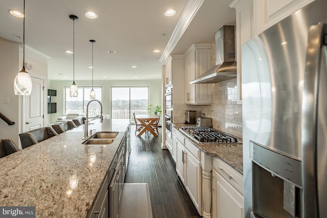 kitchen with recessed lighting, light stone countertops, a sink, wall chimney range hood, and appliances with stainless steel finishes