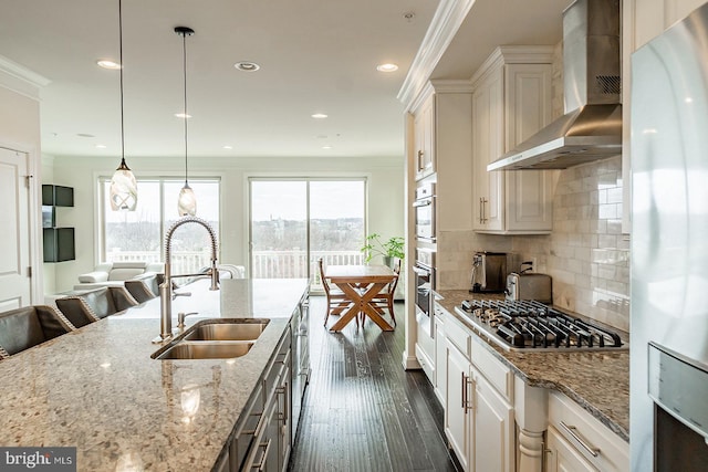 kitchen featuring a sink, stainless steel gas stovetop, wall chimney exhaust hood, light stone counters, and freestanding refrigerator