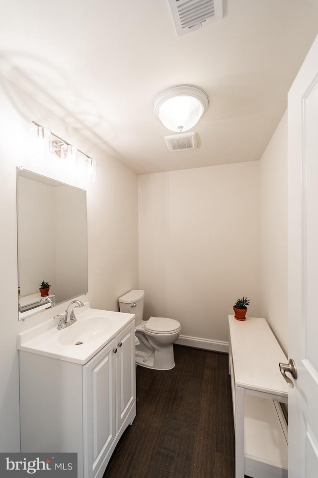 half bathroom with toilet, vanity, visible vents, and wood finished floors