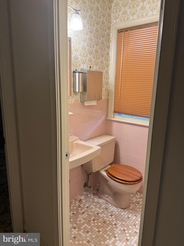half bathroom with toilet, tile walls, wallpapered walls, and tile patterned flooring