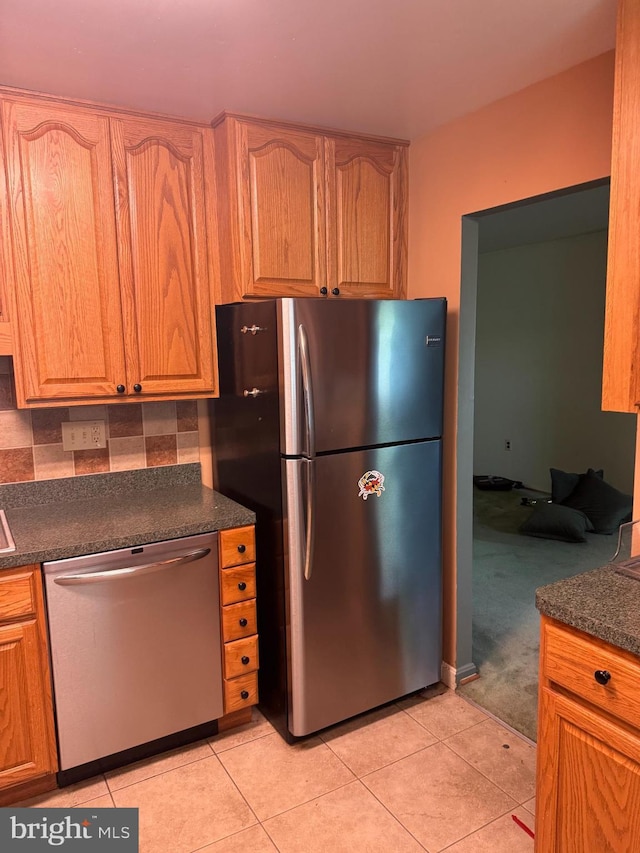 kitchen featuring light tile patterned floors, dark countertops, stainless steel appliances, and decorative backsplash