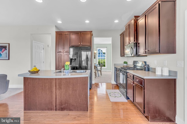 kitchen featuring a kitchen island with sink, baseboards, light countertops, light wood-style flooring, and black appliances