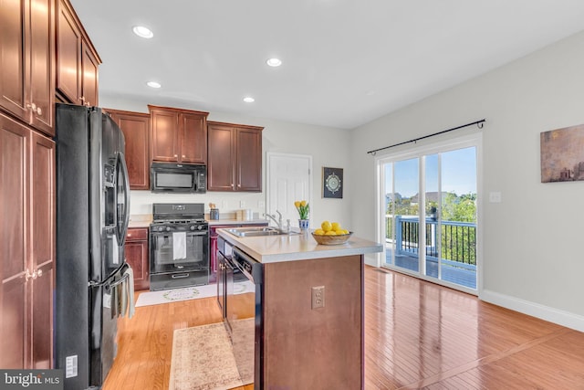kitchen with light countertops, black appliances, light wood finished floors, and a sink