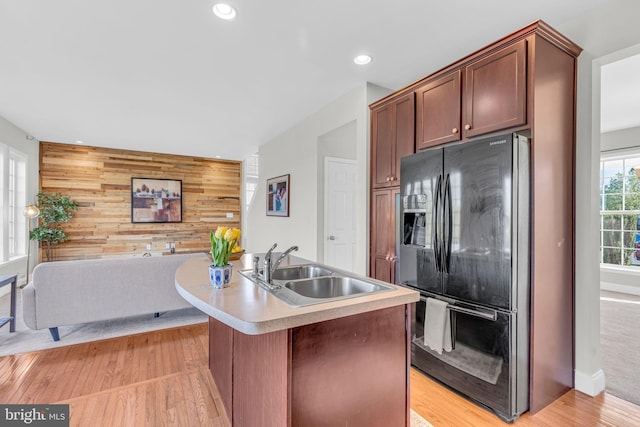 kitchen featuring wood walls, black refrigerator with ice dispenser, recessed lighting, light countertops, and a sink