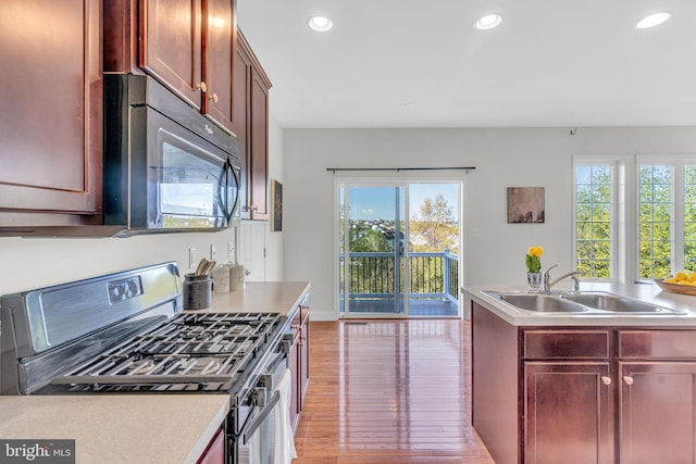 kitchen with black microwave, a sink, gas stove, reddish brown cabinets, and light wood-type flooring