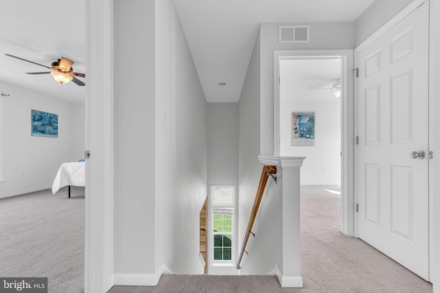 hall with carpet floors, visible vents, baseboards, and an upstairs landing