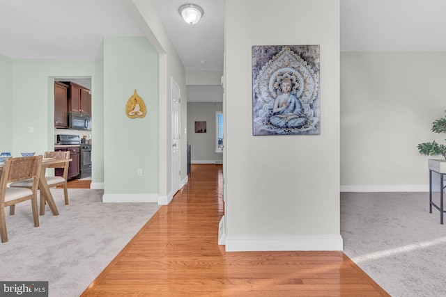 hallway featuring baseboards, light colored carpet, and light wood-style floors