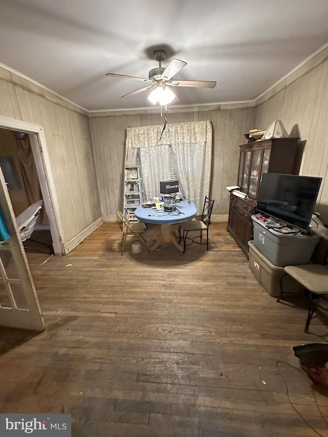 dining space with crown molding, a ceiling fan, wooden walls, and wood-type flooring