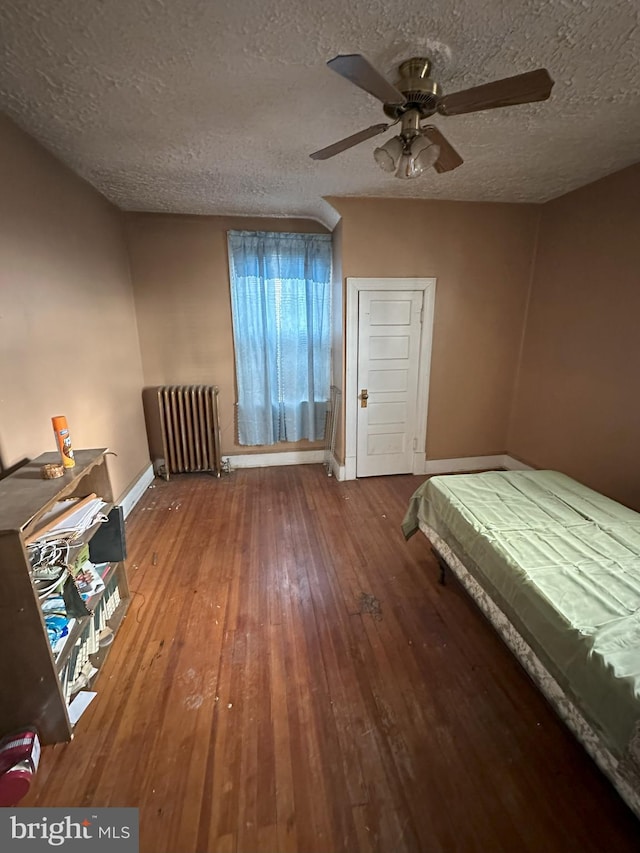 bedroom featuring a textured ceiling, hardwood / wood-style flooring, baseboards, radiator, and a ceiling fan