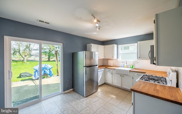 kitchen featuring a sink, butcher block countertops, visible vents, backsplash, and white appliances