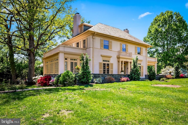 back of property featuring a yard, a chimney, stone siding, and stucco siding