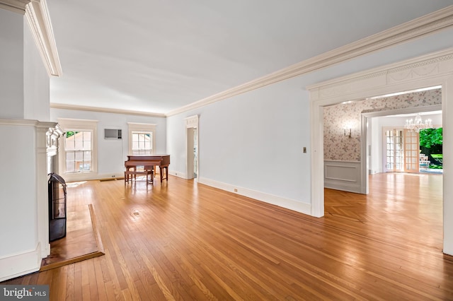 unfurnished living room with crown molding, light wood-style floors, baseboards, a wainscoted wall, and a chandelier