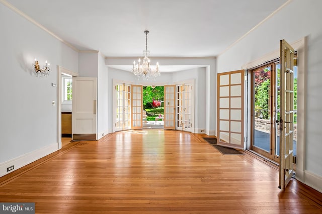 unfurnished dining area with a notable chandelier, ornamental molding, french doors, and light wood-type flooring