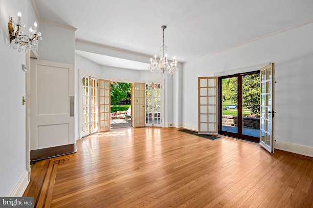 unfurnished dining area with plenty of natural light, french doors, baseboards, wood-type flooring, and a chandelier
