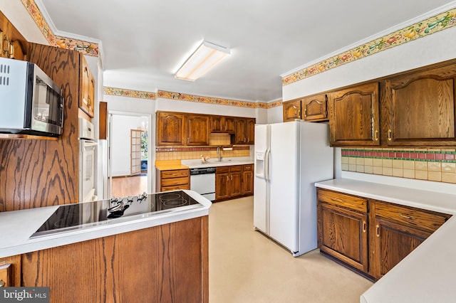 kitchen featuring a sink, white appliances, light countertops, brown cabinetry, and tasteful backsplash