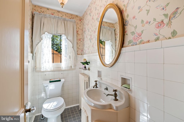 half bath with tile patterned flooring, wainscoting, tile walls, radiator heating unit, and wallpapered walls