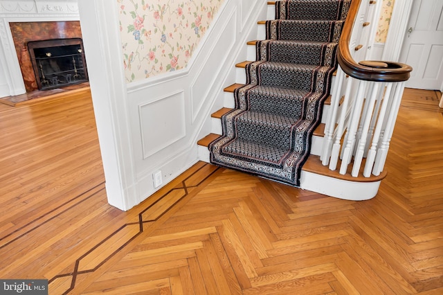 stairway with a decorative wall, a fireplace, wainscoting, and wallpapered walls