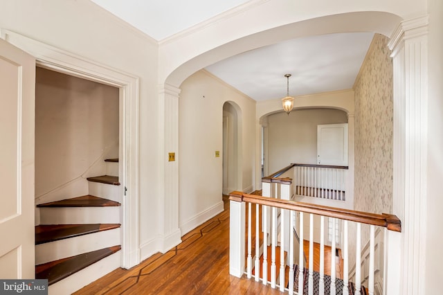 corridor with ornamental molding, wood finished floors, baseboards, arched walkways, and an upstairs landing