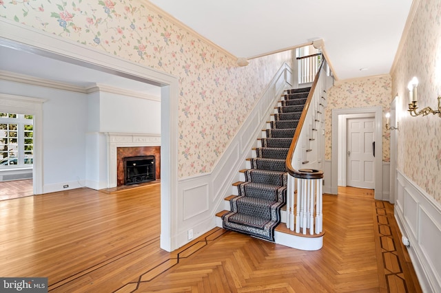 staircase with crown molding, a wainscoted wall, a decorative wall, wallpapered walls, and a premium fireplace