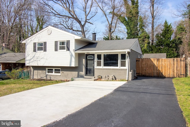 tri-level home with fence, driveway, and brick siding