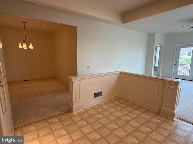 spare room with ceiling fan with notable chandelier, visible vents, light carpet, and baseboards