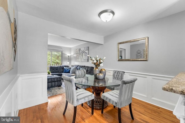 dining space with a decorative wall, wainscoting, and wood finished floors
