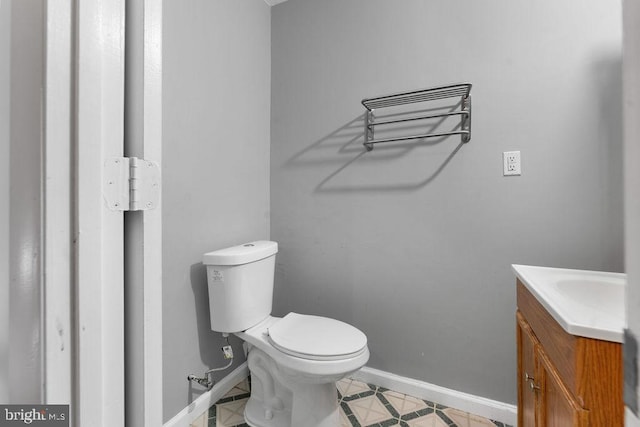 half bathroom featuring toilet, tile patterned floors, vanity, and baseboards