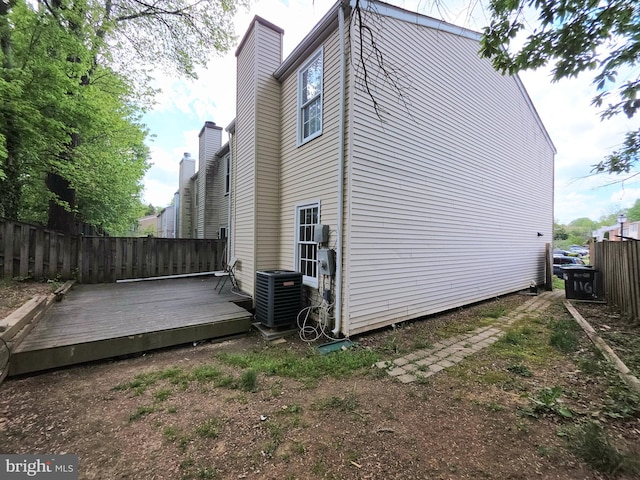 view of side of home with a chimney, central air condition unit, a wooden deck, and fence