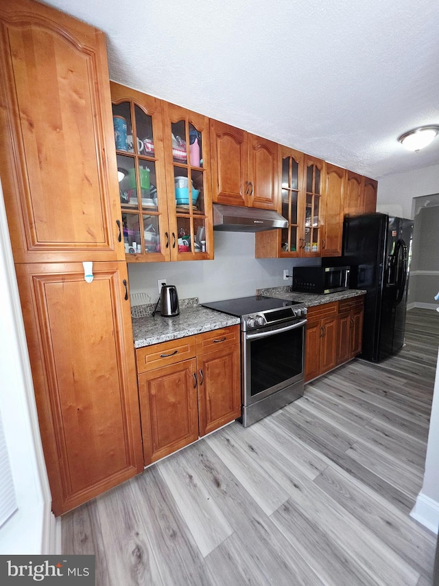 kitchen featuring brown cabinetry, electric range, black refrigerator with ice dispenser, under cabinet range hood, and light wood-style flooring