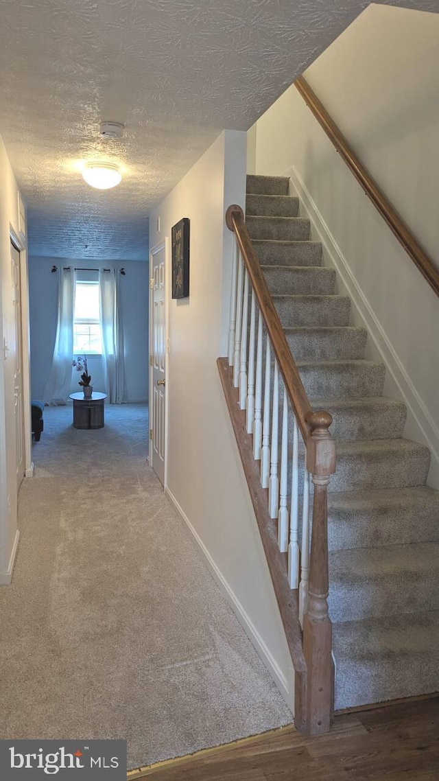 stairs with baseboards, carpet flooring, and a textured ceiling